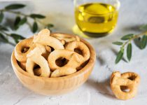 Taralli is a traditional Italian snack food typical of Puglia regional cuisine. Tarallini is in wooden bowl with olive twig. Ingredients: wine, olive oil, salt, flour of wheat
